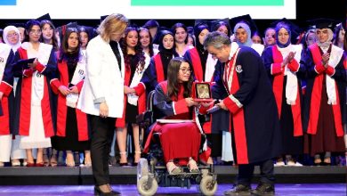 Görselde, Gaziantep Üniversitesi 2024–2025 mezuniyet töreninde, tekerlekli sandalyedeki bir öğrenciye plaket takdim ediliyor. Öğrenci kep ve cübbesiyle sahnede gururla gülümserken, akademisyenler ve diğer mezunlar alkışlarla destek veriyor. Sahne arkasında “E-Ticaret ve Pazarlama” yazısı dikkat çekiyor.