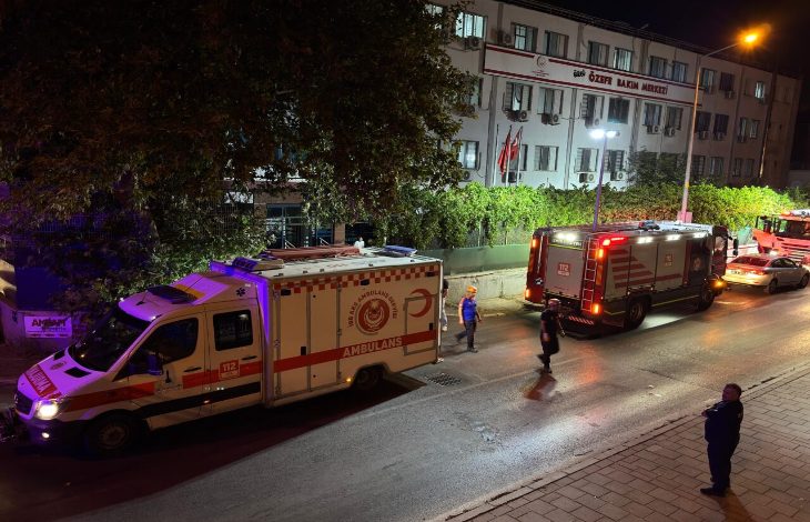 Görselde, gece saatlerinde bir özel bakım merkezinin önünde acil durum müdahalesi görülüyor. Binanın üst kısmında “Özel Bakım Merkezi” tabelası yer alıyor. Önünde bir ambulans, bir itfaiye aracı ve birkaç görevli bulunuyor. Işıklar yanıyor, sahnede bir hareketlilik var. Birkaç kişi olay yerinde görev yaparken, yol kenarında bir kişi durumu izliyor.