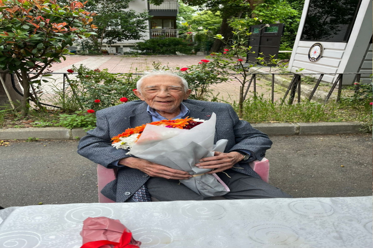 Görselde, ilerlemiş yaşı nedeniyle emekliye ayrılan Prof. Dr. Coşkun Özdemir kucağında bir buket çiçek tutuyor.