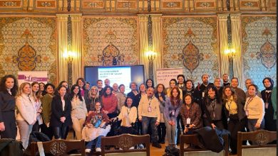 Görselde, tarihi ve gösterişli bir salonda düzenlenen bir çalıştay sonrası çekilmiş büyük bir grup fotoğrafı yer alıyor. Katılımcılar, ön planda tekerlekli sandalyedeki bireyler de dahil olmak üzere farklı yaş ve profillerden oluşuyor. Arka planda bir ekran ve yanında KASDER (Kas Hastalıkları Derneği) ile ENUYGAR logolarının yer aldığı afişler bulunuyor. Ekranda “Kas Hastalıklarında Çok Disiplinli Merkez Modelleri Çalıştayı” başlığı dikkat çekiyor.