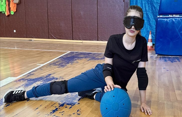 Görselde, görme engelli golbol sporcusu Fatmanur Bozkurt, bir spor salonunun zemininde topu eliyle tutarken görülüyor.