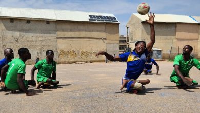 Görselde, Nijerya'nın Kano eyaletinde çekildiği anlaşılan açık hava bir alanda bedensel engelli bireyler paten futbolu oynarken görülüyor. Sporcuların bacakları yok ya da protezli, çoğu tahtadan yapılan özel kaykay benzeri düzenekler üzerinde hareket ediyor. Mavi ve yeşil forma giymiş oyuncular arasında bir oyuncu havaya zıplamış ve topa eliyle müdahale etmeye çalışıyor; yüzünde yoğun bir odaklanma ifadesi var.