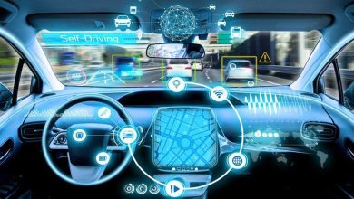 Bu görsel, bir sürücüsüz (otonom) aracın içinden ön yola bakışı gösteriyor. Direksiyon simidi ve ön panel yerinde duruyor ancak araç tamamen otomatik çalışıyor gibi görünüyor. Ön camda ve konsolda artırılmış gerçeklik (AR) grafiklerle trafik bilgileri, hız göstergeleri, sensör verileri ve harita gibi dijital veriler yansıtılmış. Özellikle navigasyon ekranı merkezde öne çıkıyor. "Self-Driving" ifadesi, bu aracın sürücüsüz olduğunu vurguluyor.