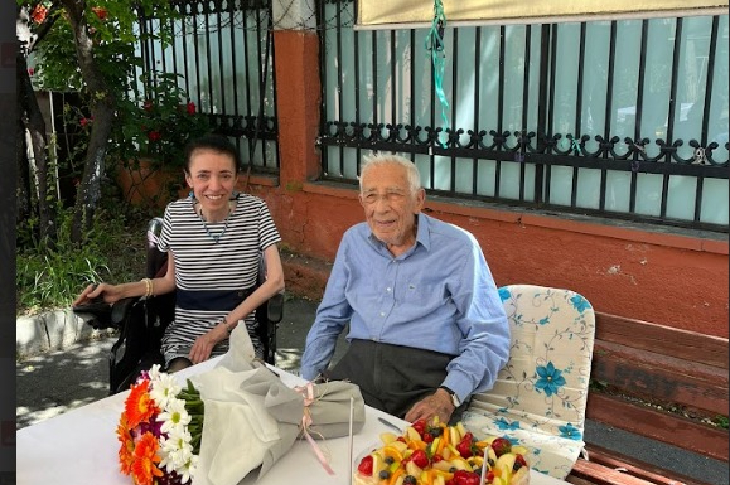 Görselde, Prof. Dr. Coşkun Özdemir ve akülü tekerlekli sandalye kullanan orta yaşlarda bir kadın ile yan yana fotoğraf için gülümseyerek poz veriyorlar.
