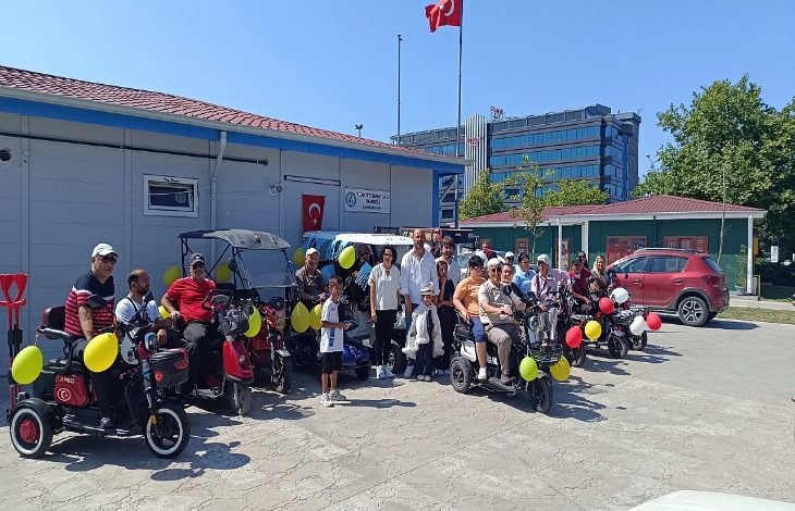 Görselde, engelli bireylerin kullandığı akülü araçların renkli balonlarla süslendiği görülmektedir. Engelli bireyler yan yana dizilerek bir tür konvoy için hazırlık yapmaktadır.