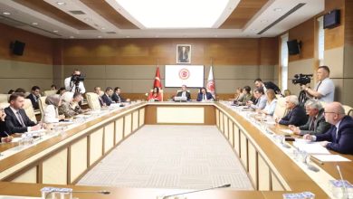 Görselde, Türkiye Büyük Millet Meclisinde gerçekleştirilen komisyon toplantısı sırasında milletvekilleri dikdörtgen biçimindeki bir masanın etrafında oturuyor. Komisyon Başkanı Mehmet Muharrem Kasapoğlu, kameranın çekim açısına göre masanın tam karşı tarafında yer alıyor.