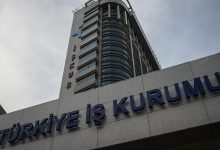 Görselde, Türkiye İş Kurumu'nun (İŞKUR) modern görünümlü yüksek binası yer almakta. Binanın ön cephesinde büyük harflerle “TÜRKİYE İŞ KURUMU” yazısı görülüyor. Üst bölümde İŞKUR’un logosu ve adı dikkat çekiyor. Fotoğraf aşağıdan yukarıya doğru çekildiği için bina oldukça heybetli bir şekilde görünüyor. Gökyüzü ise bulutlu.