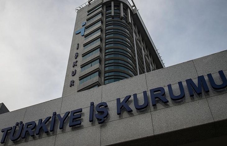 Görselde, Türkiye İş Kurumu'nun (İŞKUR) modern görünümlü yüksek binası yer almakta. Binanın ön cephesinde büyük harflerle “TÜRKİYE İŞ KURUMU” yazısı görülüyor. Üst bölümde İŞKUR’un logosu ve adı dikkat çekiyor. Fotoğraf aşağıdan yukarıya doğru çekildiği için bina oldukça heybetli bir şekilde görünüyor. Gökyüzü ise bulutlu.