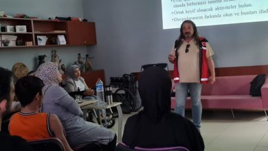 Görselde beyaz bir projeksiyon tahtasına bazı yazılar yansıtılmış ve tahtanın önünde eğitim veren bir erkek yer alıyor.