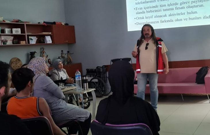 Görselde beyaz bir projeksiyon tahtasına bazı yazılar yansıtılmış ve tahtanın önünde eğitim veren bir erkek yer alıyor.