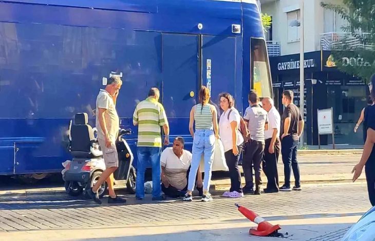 Kazanın olduğu alanda tramvay ve akülü aracın yanında yerde oturan engelli sürücünün başında vatandaşlar bulunuyor.