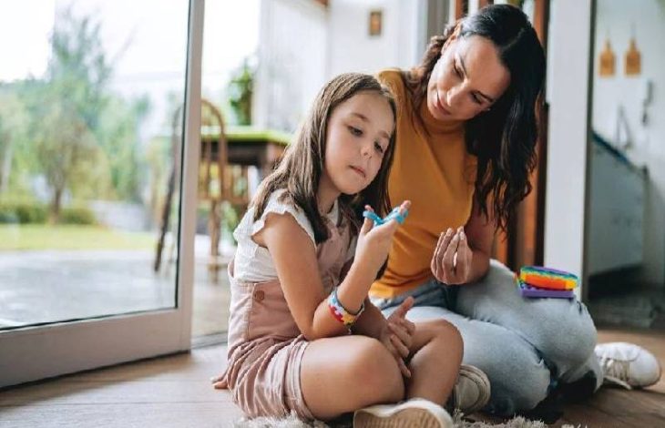 Görselde, otizm tanılı küçük bir kız çocuğu annesiyle birlikte, parmağına taktığı oyuncakla mental ve fiziksel gelişim egzersizi yapıyor.