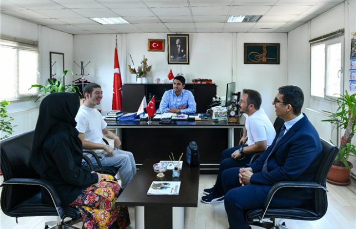 Görselde, EGO Genel Müdürlüğü odasında 5 kişilik bir grup yer alıyor. Makam koltuğunda bir kişi otururken, önünde bir engelli birey ve diğer ziyaretçiler bulunuyor.