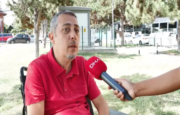 Görselde, tetraplejili engelli birey Gökhan Ayık, kırmızı renkli üzerinde “DHA” yazılı mikrofona doğru konuşuyor.