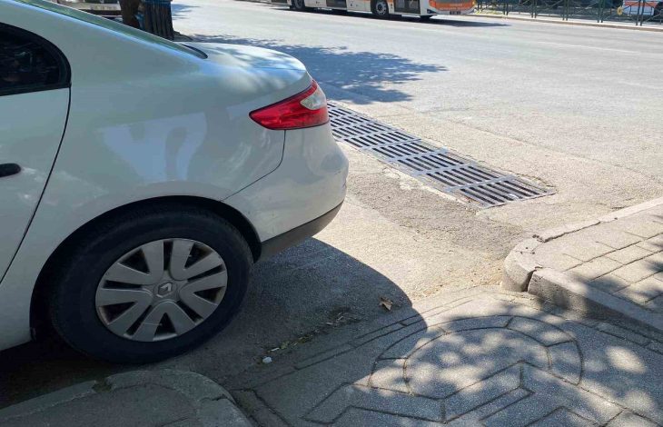 Beyaz otomobil kaldırım rampasının önünde park edilmiş.