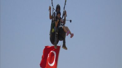 Fotoğrafta, gökyüzünde yamaç paraşütü yapan iki kişi görülüyor. Önde oturan genç kadın, arkasında ise paraşüt pilotu yer alıyor. İkilinin altında büyük bir Türk bayrağı dalgalanıyor. Arka plan tamamen mavi gökyüzünden oluşuyor.