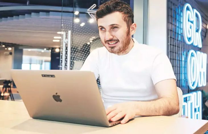 Görselde, görme engelli birey Atakan Nalbant ofis ortamı gibi bir yerde masanın üzerine katmış olduğu laptop bilgisayarıyla çalışırken fotoğrafı çekilmiş.