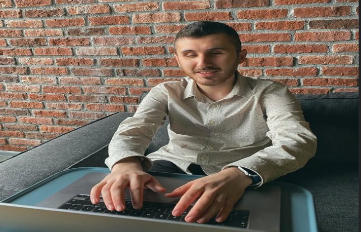 Görselde Binclusive sosyal girişimin kurucusu Atakan Nalbant, önünde yer alan dizüstü bilgisayarı bir masa üzerinde kullanıyor.