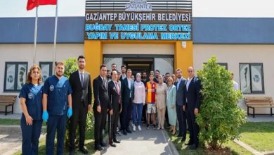 Görselde, Gaziantep Büyükşehir Belediyesi’ne ait “Buğday Tanesi Protez Ortez Yapım ve Uygulama Merkezi” önünde toplanmış kalabalık bir grup yer alıyor. Kadın ve erkeklerden oluşan ekip, resmi kıyafetli yetkililer, sağlık personelleri ve sivil vatandaşlardan oluşuyor. Ortada, Galatasaray forması giyen bir çocuk ve ailesi bulunuyor; büyük olasılıkla protez kol uygulaması yapılan çocuk bu. Arka planda merkezin adı tabelada mavi harflerle yazılı.