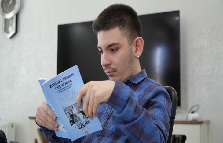 Görselde genç bir erkek Mert Esat Ölmez, mavi kareli bir gömlek giymiş şekilde elindeki açık kitabı dikkatle okuyor. Kitabın kapağında “Zorluklardan Güç Almak” yazıyor. Arka planda televizyon ve ev ortamına ait eşyalar görünüyor.