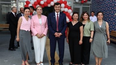 Görselde, Kütahya Belediyesi tarafından hayata geçirilen “Yamantürk Yaşlı ve Engelli Gündüz Yaşam Merkezi”nin açılış töreninden bir kare yer alıyor. Ön planda altı kişi – dört kadın, bir erkek ve bir kadın daha – resmi bir duruşla kameraya poz veriyor. Hepsi şık giyimli ve gülümseyerek açılışın coşkusunu yansıtıyor. Arkada kırmızı-beyaz balonlardan oluşan bir kemer, binanın girişini süslüyor.