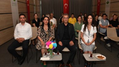 Görselde, bir seminer salonunda düzenlenen etkinlikte ön sırada oturan dört kişi kameraya bakarak poz veriyor. Masalarda çaylar, kurabiyeler ve çiçekler bulunuyor. Arka planda ise katılımcılar sıralı şekilde oturmuş, dikkatle etkinliği izliyorlar. Duvarlarda Osmangazi Belediyesi logoları ve Türk bayrakları yer almakta. Ortam resmi ve düzenli, "Engellilik ve Kentsel Yaşam" temalı bir seminere ait.