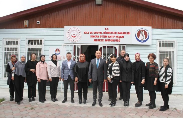 Görselde, T.C. Aile ve Sosyal Hizmetler Bakanlığı Sincan Otizm Aktif Yaşam Merkezi Müdürlüğü binasının önünde poz veren bir grup insan yer alıyor. Aralarında kadınlar ve erkekler bulunan yaklaşık 14 kişilik grup, ön kapının önünde sıralanmış halde kameraya bakarak gülümsüyor. Bina ahşap çatılı, açık mavi renkli prefabrik bir yapı. Girişin üstünde kurumun ismini belirten bir tabela bulunuyor.