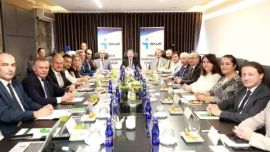 Görselde, uzun bir toplantı masası etrafında toplanmış kalabalık bir grup görülüyor. Katılımcılar resmi kıyafetler içinde ve çoğu ciddi bir ifadeyle kameraya bakıyor. Masada su şişeleri, meyve tabakları, not defterleri ve isimlikler yer alıyor. Arka planda “İŞKUR” logolu iki pano ile “Samsun Çalışma ve İş Kurumu İl Müdürlüğü” yazıları dikkat çekiyor.