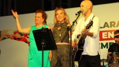 Görselde, sahnede üç kişi mikrofon önünde yer alıyor. Bir kadın yeşil elbiseyle el sallarken, ortadaki kadın gülümseyerek izleyiciye bakıyor. Yanlarında Murat Evgin ise gitar çalıyor ve şarkı söylüyor. Arka planda davulcu ve etkinlik afişinin bir kısmı görünüyor.