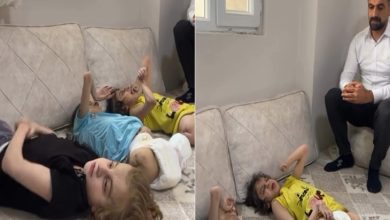 Görsel iki kareden oluşuyor. Soldaki karede, evin oturma odasında yere serilmiş minderlerin üzerinde yatan, farklı renklerde tişört giymiş üç çocuk görülüyor. Çocuklardan ikisi sarı, biri mavi tişört giyiyor ve hepsi hareketsiz şekilde uzanıyor. Sağdaki karede ise aynı çocuklar yine minderlerin üzerinde yatarken, yanlarında beyaz gömlek giymiş, siyah pantolonlu bir adam oturuyor. Adam ciddi bir ifadeyle çocuklara bakıyor.