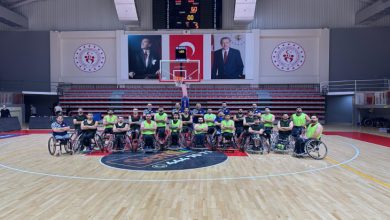 Spor salonunun basketbol sahasında Tekerlekli Sandalye Basketbol A Milli Takımı oyuncularından oluşan kalabalık bir grup poz veriyor. Arka planda tribünler yer almakta ve duvarda Türkiye Cumhuriyeti'nin resmi amblemleri, Atatürk'ün ve Cumhurbaşkanı Recep Tayyip Erdoğan'ın büyük portreleri ile birlikte bir skor tabelası dikkat çekiyor.