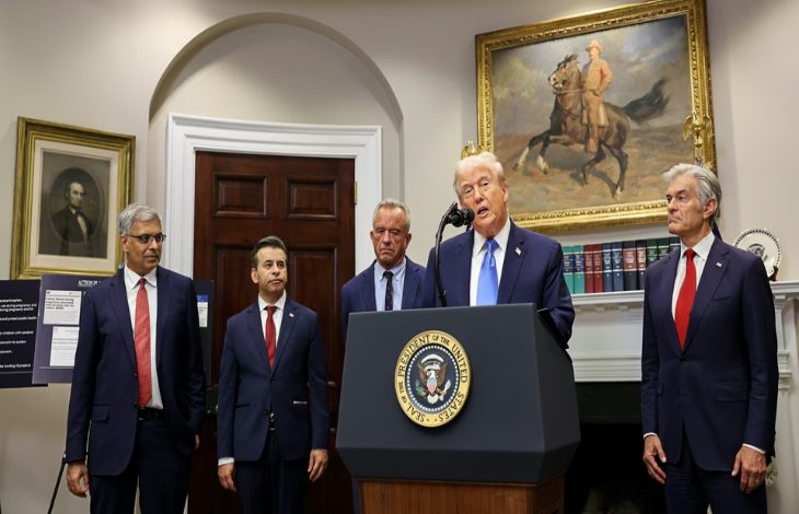 Görselde, ABD Başkanı kürsüde konuşma yapıyor. Kürsünün üzerinde ABD Başkanlık mührü yer alıyor. Yanında takım elbiseli dört erkek bulunuyor. Arka planda kitaplık, kapı ve duvarda asılı tablolar (biri at üstünde asker figürü, diğeri bir portre) dikkat çekiyor. Fotoğraf, resmi bir açıklama sırasında çekilmiş.