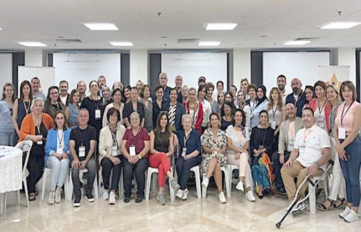 Görselde, bir konferans salonunda düzenlenen toplu bir etkinlikte, farklı yaş ve cinsiyetten yaklaşık 60 kişilik bir grup kameraya poz veriyor. Ön sırada oturanlar, arka sırada ise ayakta duran katılımcılar bulunuyor. Katılımcıların boyunlarında yaka kartları takılı; bu, etkinliğin resmi bir çalıştay veya zirve olduğunu gösteriyor. Fotoğraf, “Bağımsız Yaşam ve Eşitlik” temalı bir çalıştaya katılanların birlikte verdiği güçlü bir birliktelik pozunu yansıtıyor.