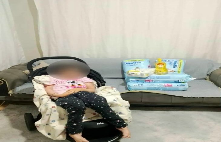 Fotoğrafta bir ev ortamında, bebek arabasına benzer bir koltukta oturan bir kişi yer alıyor. Yüzü bulanıklaştırılmış. Arka planda bir koltuk üzerinde çocuk bezi ve bakım malzemeleri görülüyor. Görüntü, yardım ya da bağış temalı bir durumu yansıtıyor.