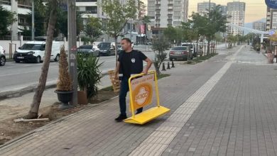 Erkek zabıta personeli sarı şeritli görme engelli yolunun üzerinde bulunan reklam panosunu kaldırıyor.