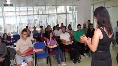 Kadın eğitmen kurs salonunda sandalyeler bulunan EKPSS kursiyerlerine ders anlatıyor.