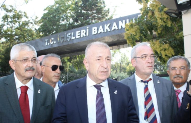 Fotoğrafta, Zafer Partisi Genel Başkanı Ümit Özdağ ve beraberindeki heyet, T.C. İçişleri Bakanlığı tabelasının önünde basın açıklaması yapar pozisyonda görülüyor. Grup takım elbiseli, ciddi ifadelerle kameraya bakıyor. Arka planda yeşil ağaçlar ve bakanlık giriş kapısı dikkat çekiyor.