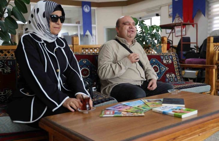 Geleneksel motiflerle süslenmiş bir oturma alanında görme engelli yazar Selman Devecioğlu ile eşi yan yana oturuyor. İkisi de gülümseyerek sohbet ederken, önlerindeki masada birkaç kitap ve çay bardağı bulunmaktadır. Arka planda ise ofis ya da sosyal tesis havası veren bir iç mekân görünmekte, duvarlarda çeşitli bayraklar ve afişler yer almaktadır.