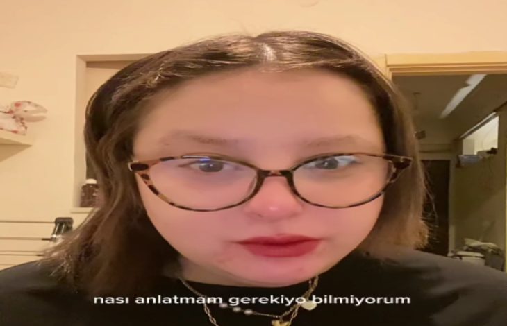 Görselde, gözlüklü bir kadın iç mekânda kameraya doğru bakıyor. Üzerinde siyah bir giysi var. Görüntünün alt kısmında “nası anlatmam gerekiyo bilmiyorum” yazısı yer alıyor.