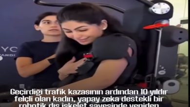 Bir kadın, yapay zekâ destekli robotik bir dış iskelet yardımıyla ayakta duruyor. Yanında ona destek olan bir görevli bulunuyor. Kadın gülümseyerek duygusal bir an yaşıyor. Alt kısımda, kazadan sonra 10 yıl boyunca felçli kaldığı ve bu teknolojiyle yeniden yürümeyi başardığı yazılı.
