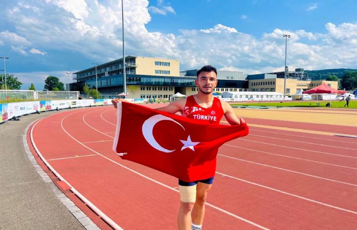 Milli sporcumuz Abdullah Ilgaz, tartan pistte Türk Bayrağı tutarak poz veriyor.