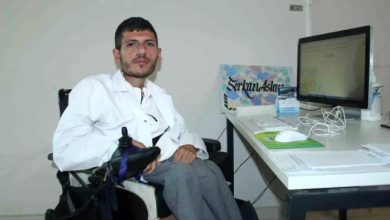 Psikolog Serkan Arslan, akülü sandalyede oturarak bilgisayar bulunan çalışma masasında poz veriyor.