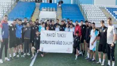 Görselde futbol sahasında bir grup sporcu ve genç birlikte poz veriyor. Ellerinde “Haydi Tunceli Koruyucu Aile Olalım” yazılı bir pankart tutuyorlar. Arka planda tribünler ve saha düzeni görülüyor. Katılımcılar gülümseyerek kameraya bakıyor.