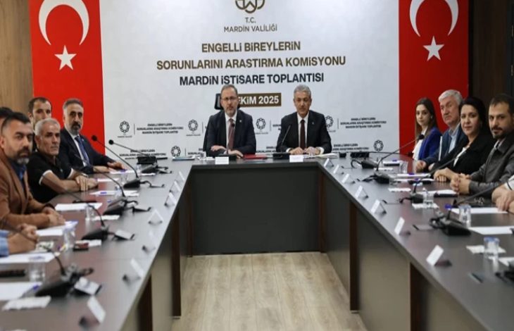 Görselde uzun bir toplantı masası etrafında oturmuş kişiler görülüyor. Masanın başında iki erkek konuşmacı yer alıyor. Arkadaki duvarda “T.C. Mardin Valiliği – Engelli Bireylerin Sorunlarını Araştırma Komisyonu Mardin İstişare Toplantısı – Ekim 2025” yazısı ve iki yanda Türk bayrakları bulunuyor.