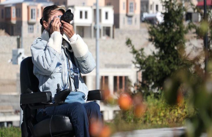 Dilek Çimen, tekerlekli sandalyesinde bulunarak fotoğraf çekiyor.
