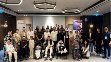 Bir toplantı salonunda, çoğunluğu ailelerden oluşan kalabalık bir grup birlikte poz veriyor. Ön sırada tekerlekli sandalyede ve bebek arabasında çocuklar bulunuyor.