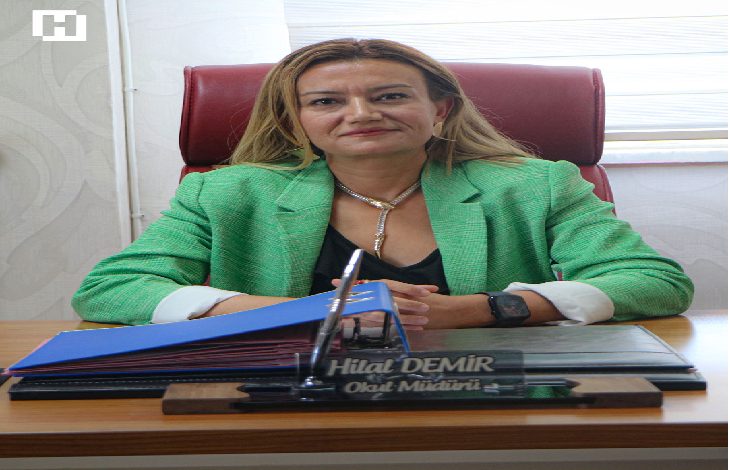 Yeşil ceketi ve kararlı duruşuyla okul müdürü Hilal Demir, bordo koltuğunda otururken önündeki isimlik, klasörler ve düzenli masa düzeni onun disiplinli, güçlü ve ilham veren bir eğitimci olduğunu tek karede hissettiriyor.