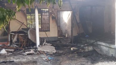 Görselde yangın sonrası ağır hasar almış bir ev görülüyor. Duvarlar ve tavan islerle kaplanmış, bazı bölümler tamamen yanmış durumda. Kapı açık, pencerelerin demir parmaklıkları kararmış. Avluda yıkılmış sütun parçaları, yanmış mobilyalar ve kül olmuş eşyalar yer alıyor. Genel atmosfer, bir yangın felaketinin ardından oluşan yıkımı yansıtıyor.