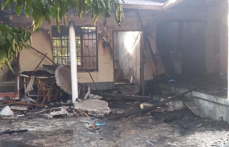 Görselde yangın sonrası ağır hasar almış bir ev görülüyor. Duvarlar ve tavan islerle kaplanmış, bazı bölümler tamamen yanmış durumda. Kapı açık, pencerelerin demir parmaklıkları kararmış. Avluda yıkılmış sütun parçaları, yanmış mobilyalar ve kül olmuş eşyalar yer alıyor. Genel atmosfer, bir yangın felaketinin ardından oluşan yıkımı yansıtıyor.