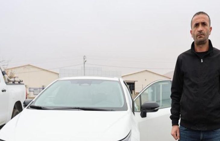 Fatih Tuğ beyaz renkli otomobilinin yanında ayakta duruyor.